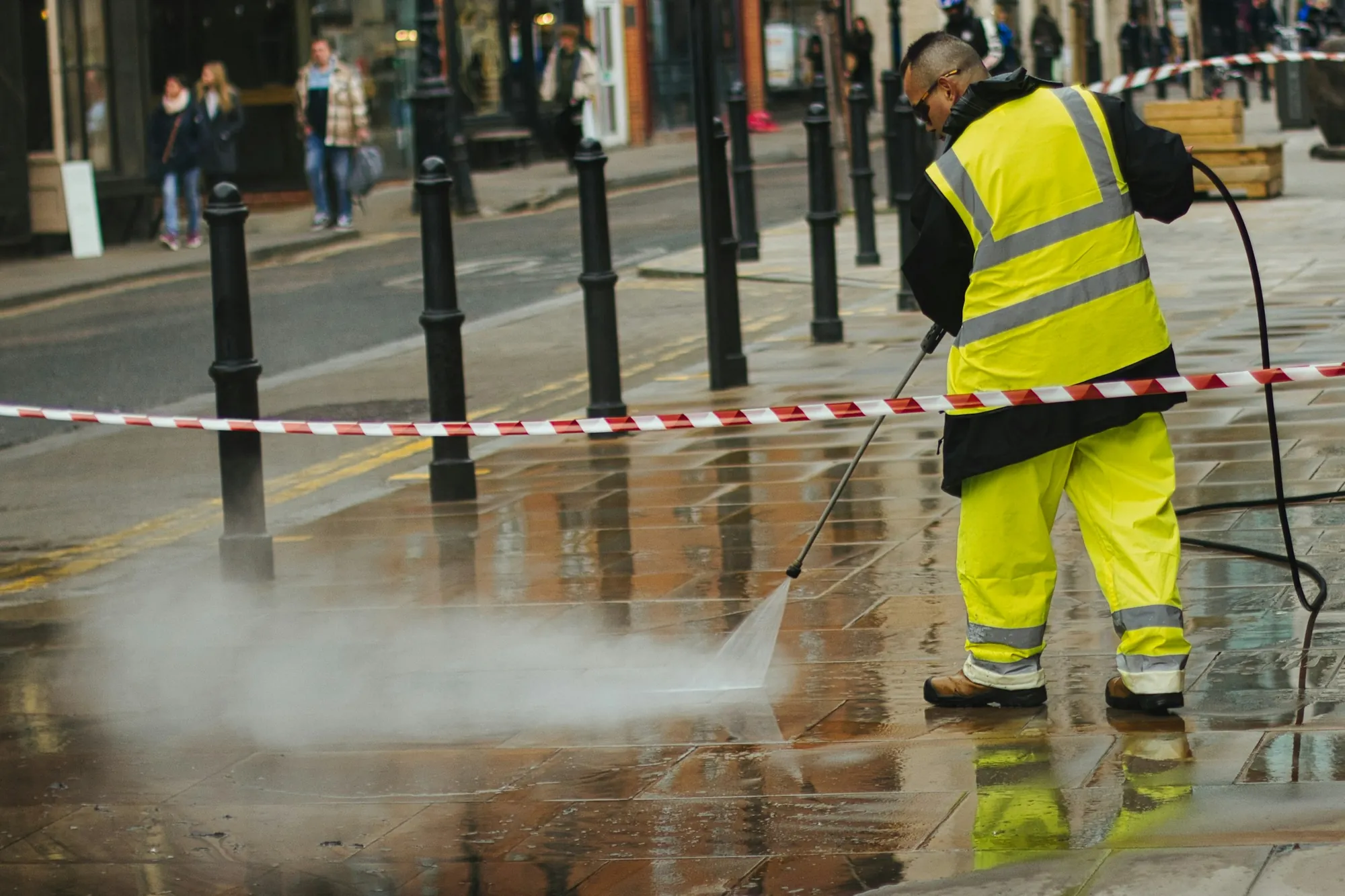 Technician in high-visibility gear pressure washing a paved street